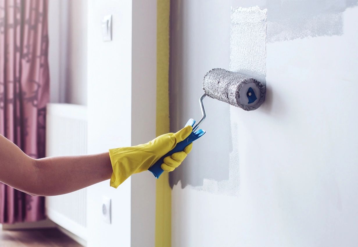 a hand painting a wall with roller brush